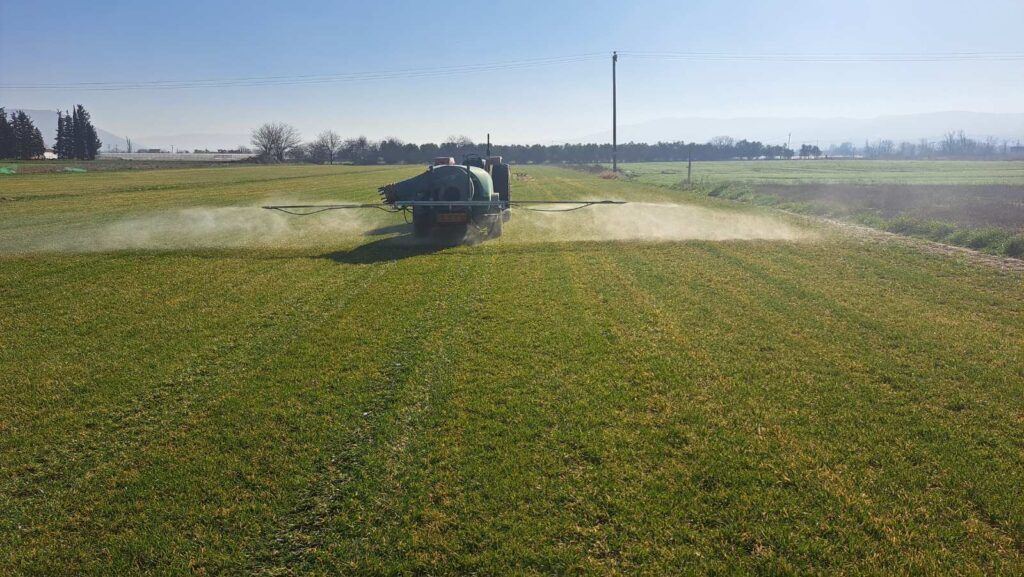 Tractor-mounted crop sprayer dispersing a fine mist over a green field on a sunny day