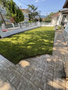 A landscaped backyard with a green lawn bordered by a white fence and a tiled patio on the right side of the yard.
